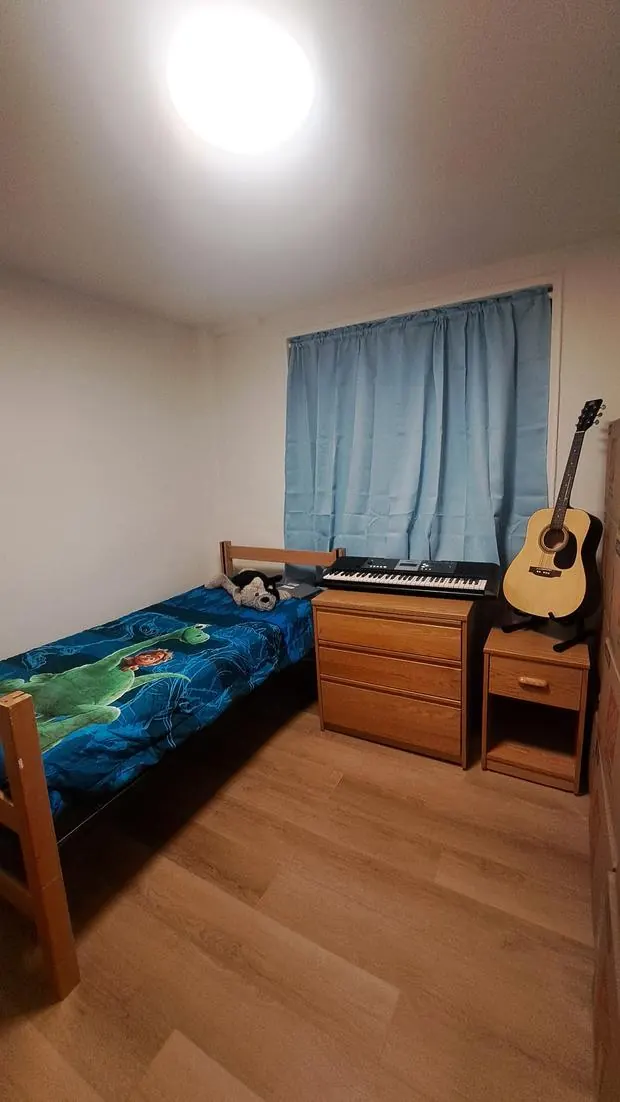 A child's bedroom with a twin bed, dinosaur comforter, oak dresser, nightstand, keyboard, and guitar